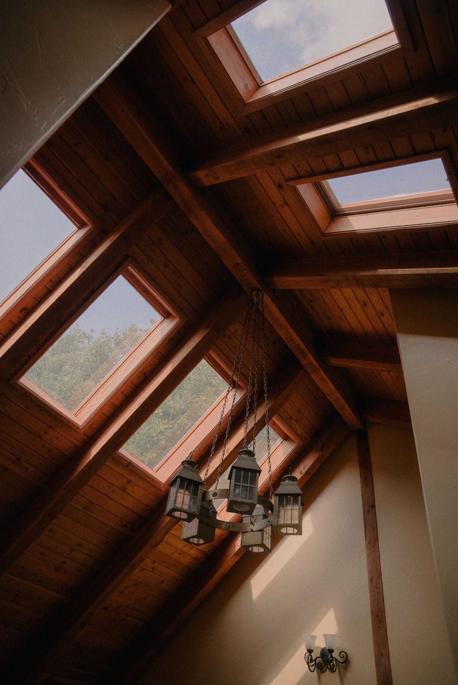 Warm rustic interior showing a wooden ceiling with skylights and lantern chandeliers, creating a cozy atmosphere.
