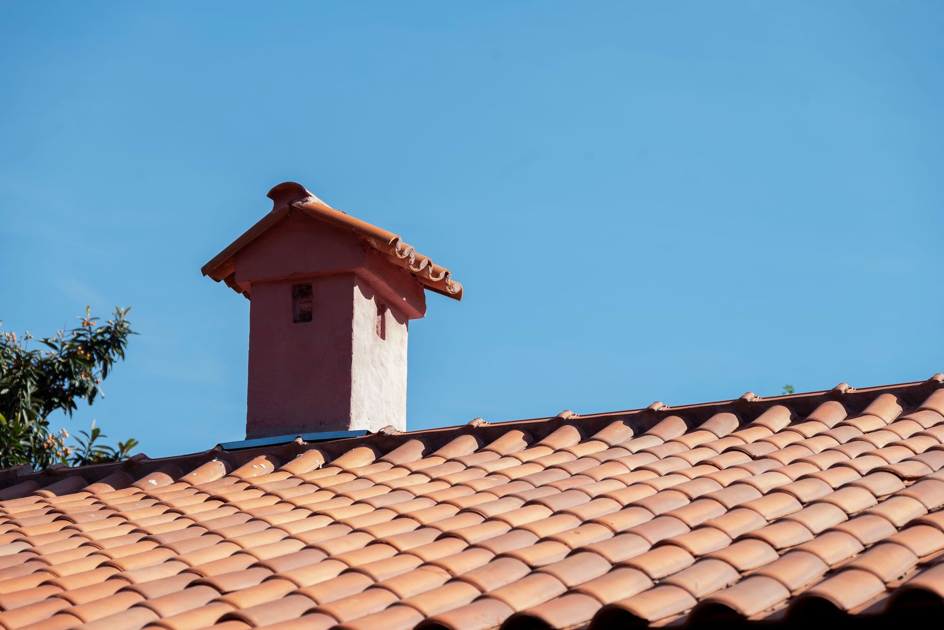 Close-up of a red tiled roof and chimney under a bright blue sky, showcasing vibrant architectural detail.